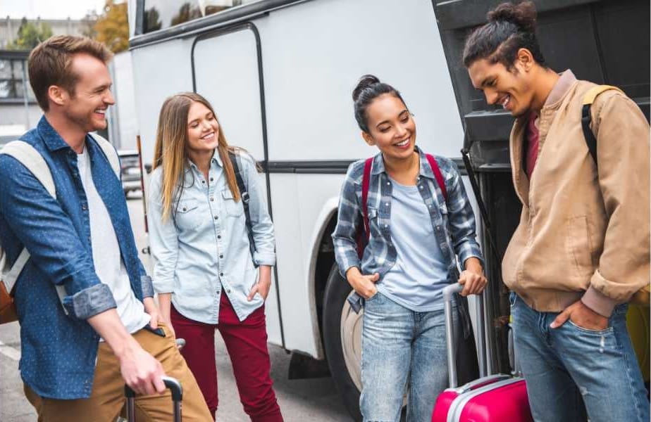 Laughing multi-ethnic tourists with travel bags loading into coach hold